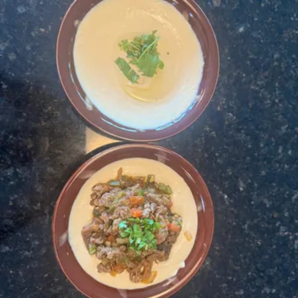 Two bowls of creamy hummus, one topped with cilantro, the other with seasoned meat and vegetables.