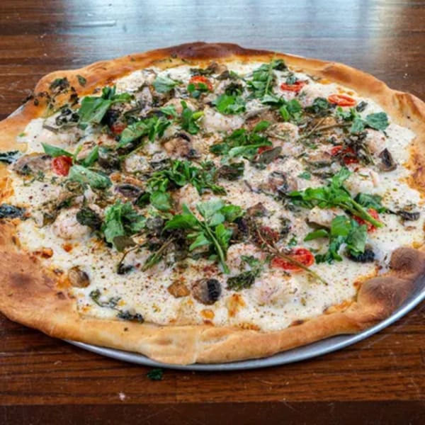 A white pizza from Blue Eye Bistro, topped with mushrooms, tomatoes, and fresh greens.