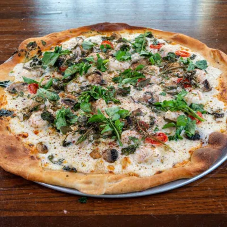 A white pizza from Blue Eye Bistro, topped with mushrooms, tomatoes, and fresh greens.