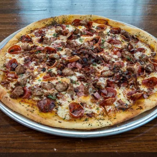 A large, round Blue Eye Bistro meat lover's pizza with pepperoni, sausage, and ham on a metal tray.