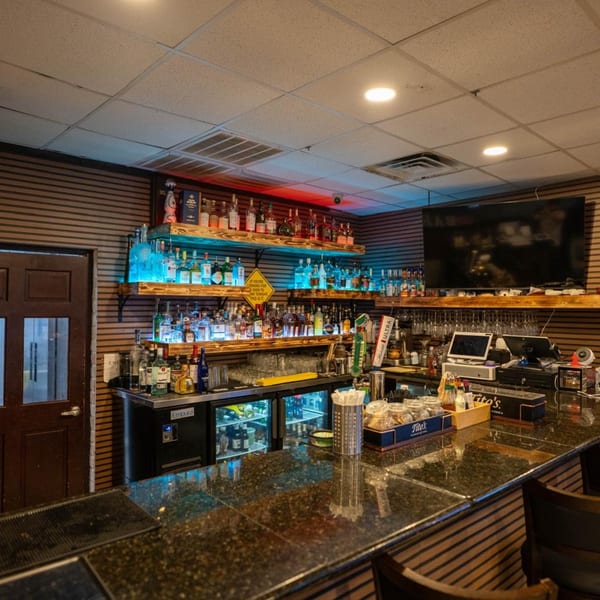 A well-stocked bar at Blue Eye Bistro with liquor bottles on illuminated shelves and a dark granite countertop.