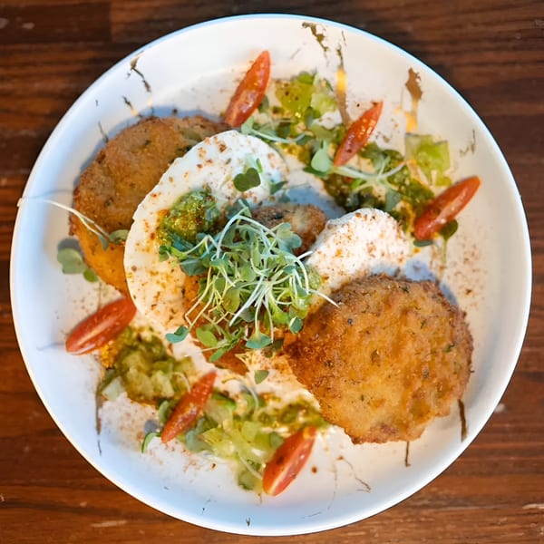 Fried green tomatoes with burrata, pesto, microgreens, and sliced cherry tomatoes on a white plate.