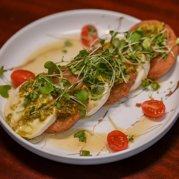 Fried green tomatoes topped with fresh mozzarella, pesto, microgreens, and cherry tomatoes.