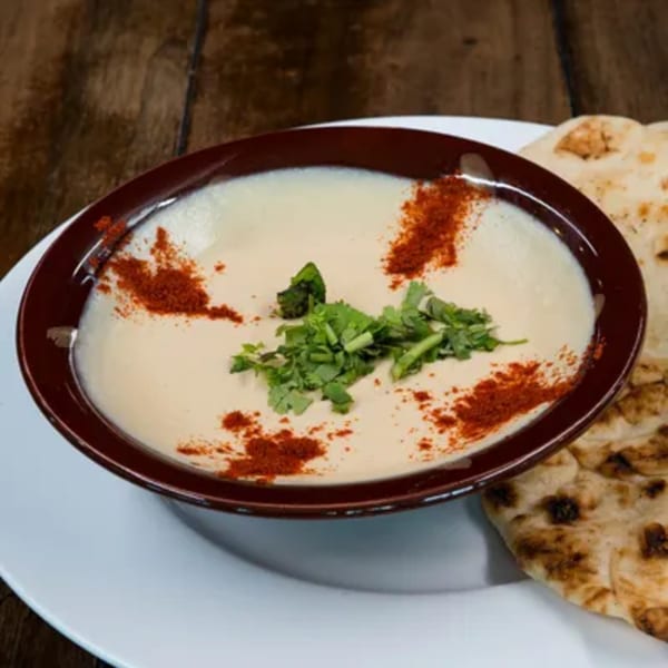 Hummus topped with paprika and cilantro, served with naan bread on a white plate.