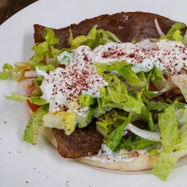 A Blue Eye Bistro gyro with meat, lettuce, white sauce, and red spice on a white plate.
