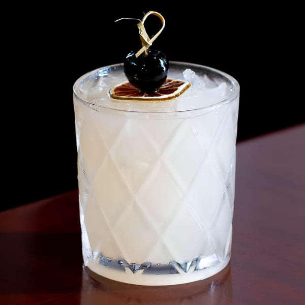 Blue Eye Bistro cocktail, light-colored drink in a textured glass with a dark cherry and dried citrus.