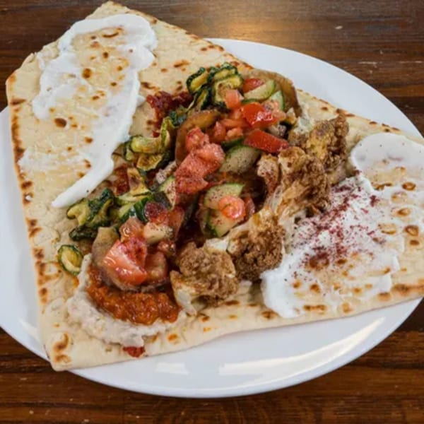 Flatbread topped with hummus, roasted vegetables, fried cauliflower, and yogurt sauce.