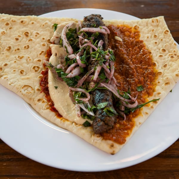 A Blue Eye Bistro kebab wrap with hummus, red sauce, onions, and parsley on a white plate.