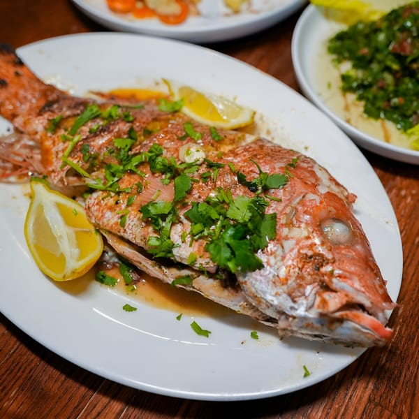 Whole roasted red snapper with lemon wedges and fresh parsley on a white platter.