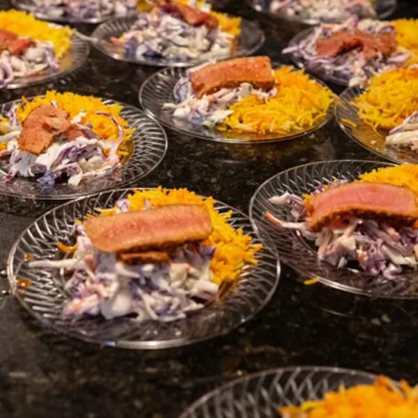 Multiple plates of seared tuna with coleslaw and shredded yellow cheese on a dark counter.