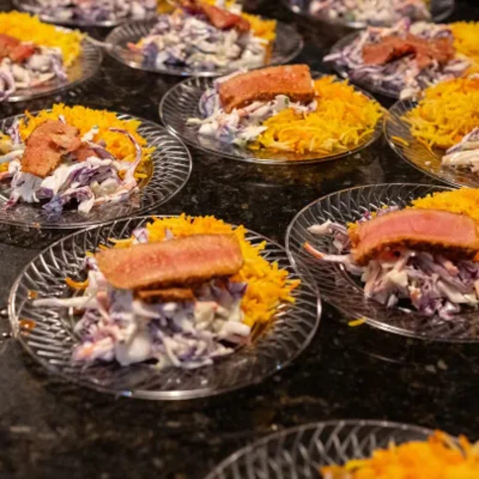 Multiple plates of seared tuna with coleslaw and shredded yellow cheese on a dark counter.