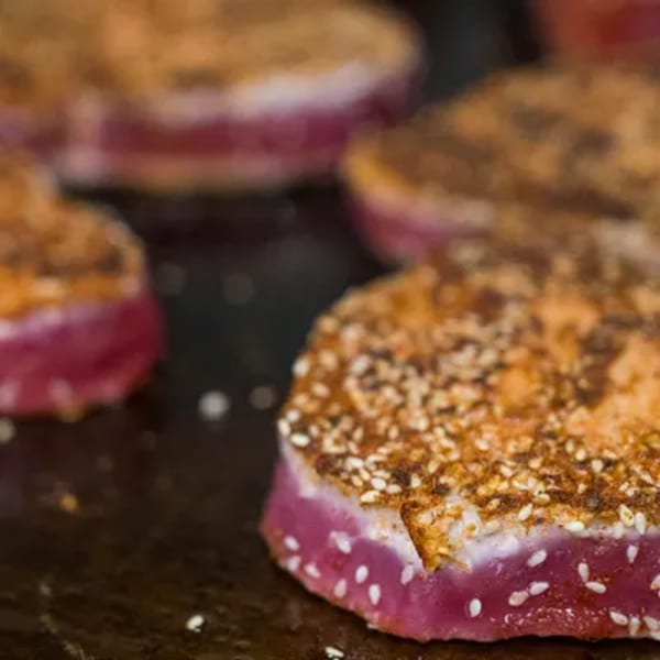 Seared tuna steaks with a sesame seed crust and pink centers cooking on a grill.
